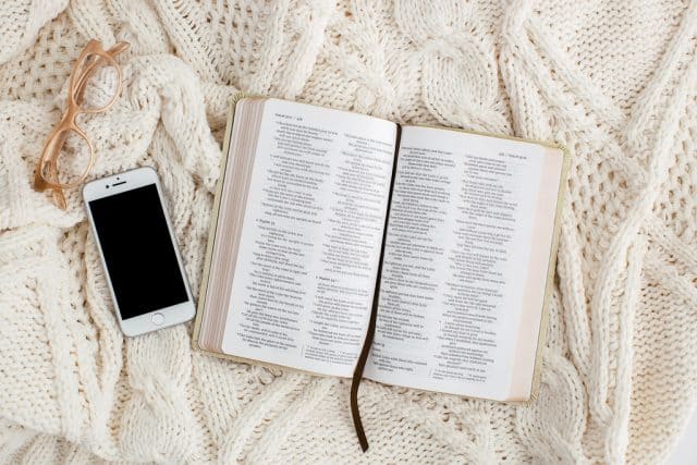 open Bible on a white blanket with a cell phone and glasses