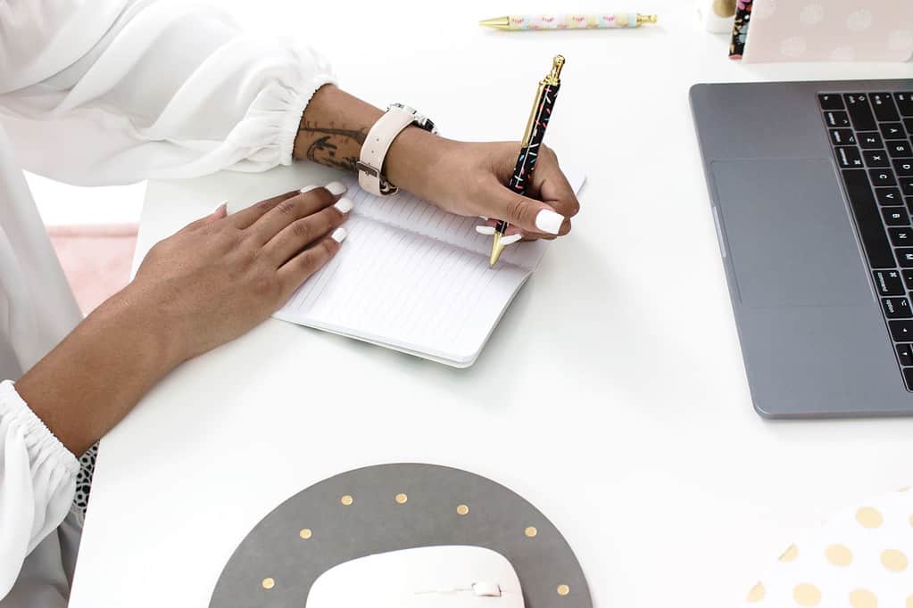 woman writing at desk with gray computer and mouse pad