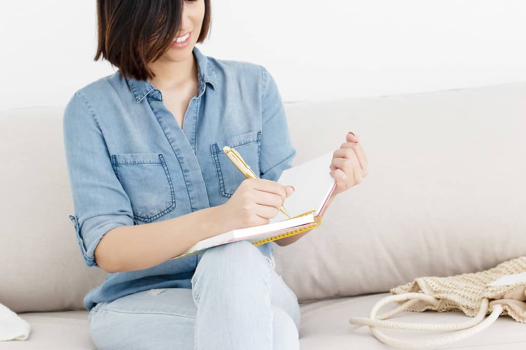 woman writing in her prayer journal on the couch