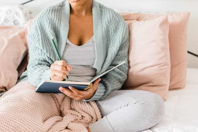  niña escribiendo en el diario de oración en la cama