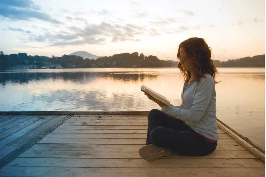 woman reading Bible verses of hope on the dock at sunrise