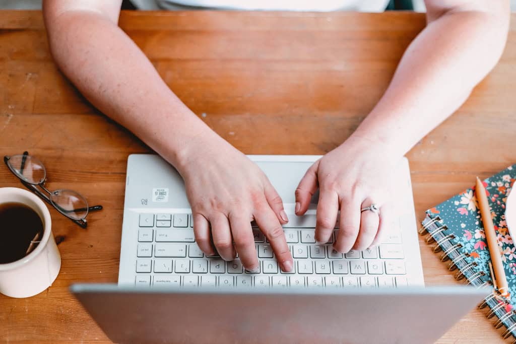 woman's hands working at the computer with coffee and journal